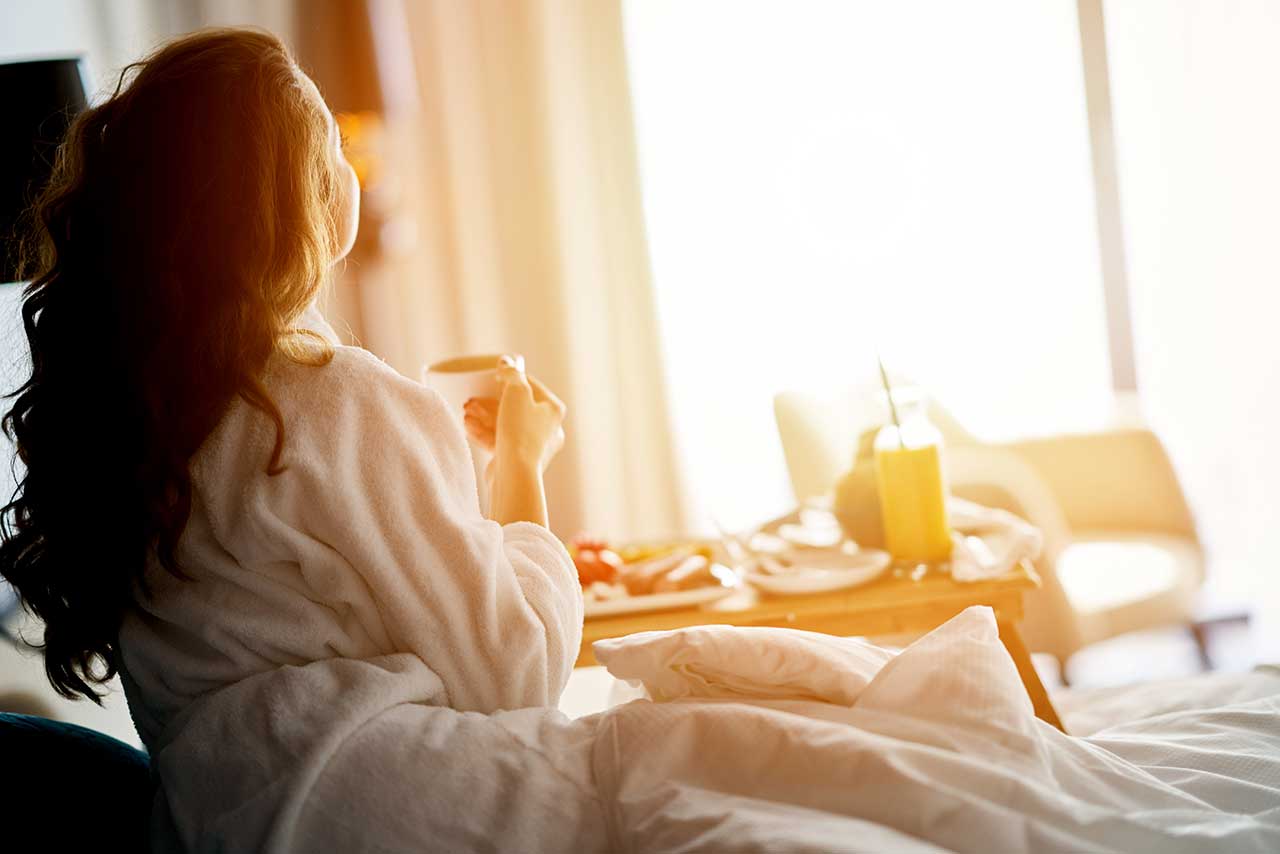 Woman has breakfast in bed in a cozy hotel room