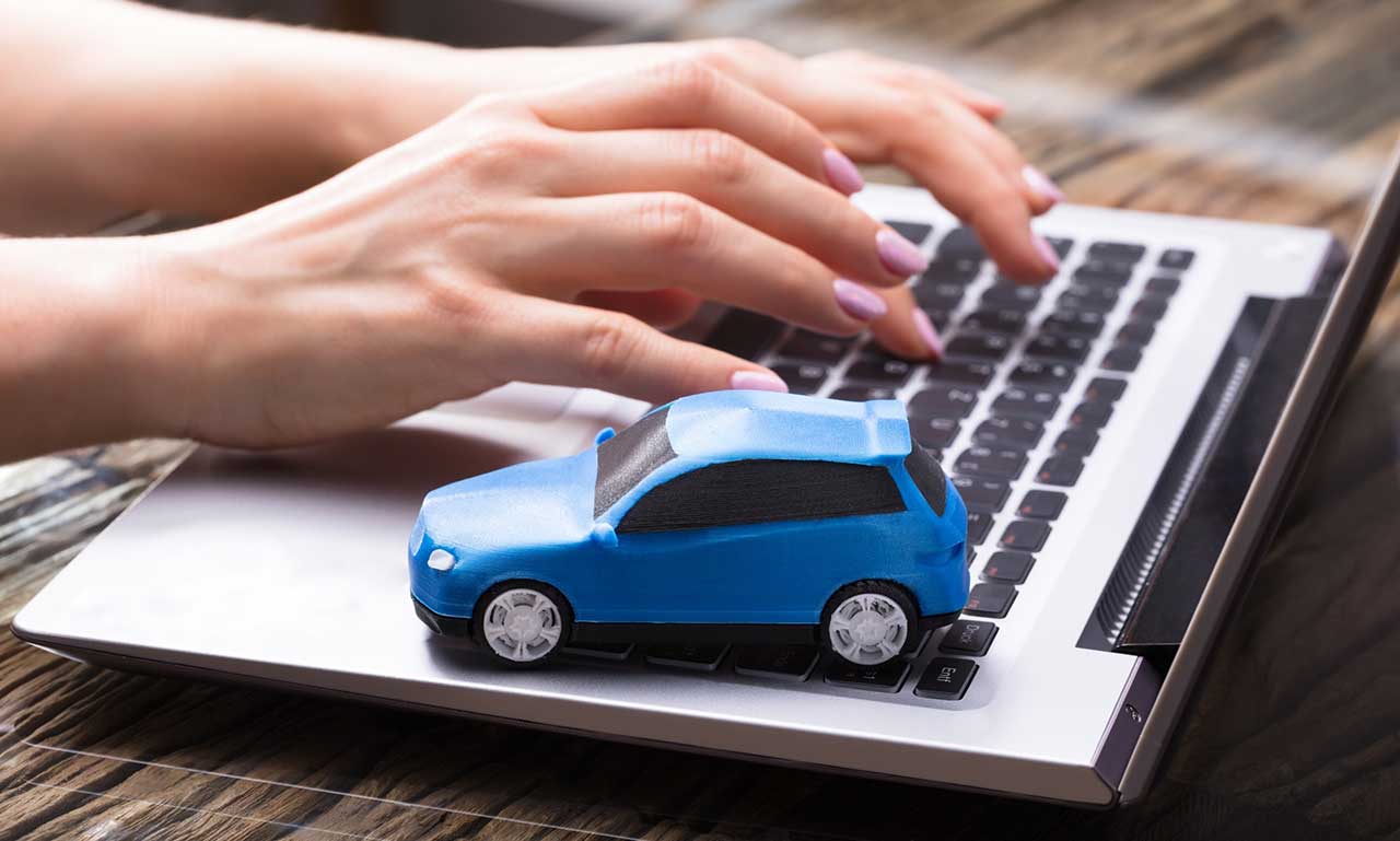 Detail of hands typing on the computer keyboard with a small blue car model next to it