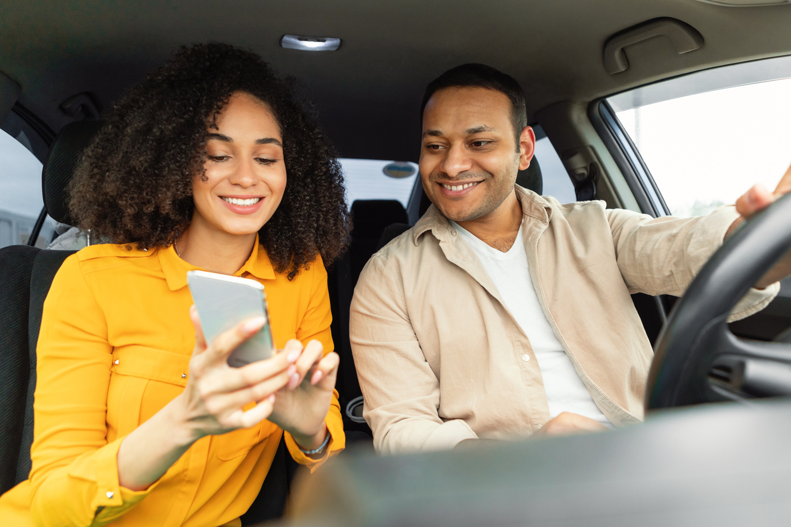Cheerful spouses driving car using cellphone