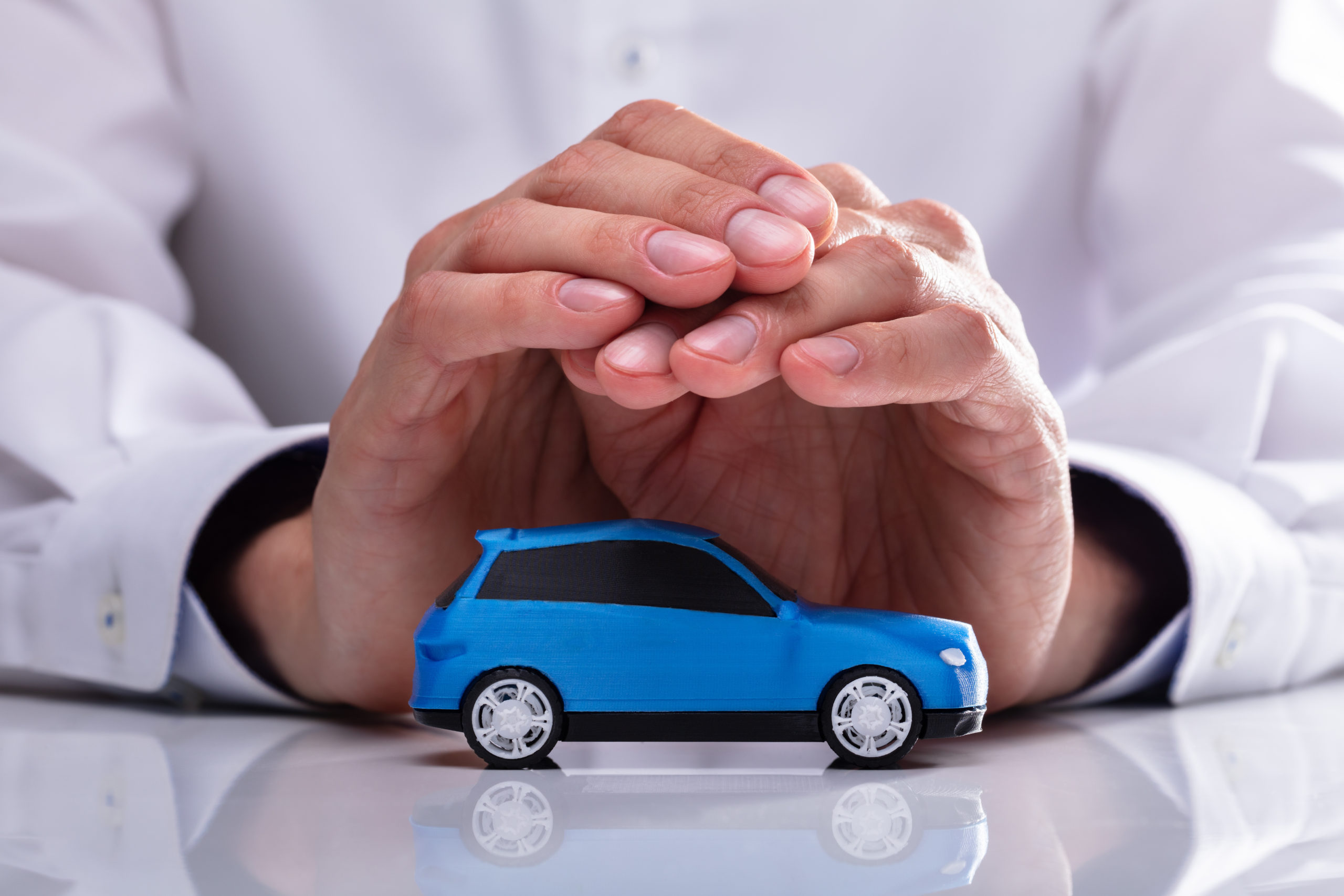 Businessman's Hand Protecting Small Miniature Blue Car