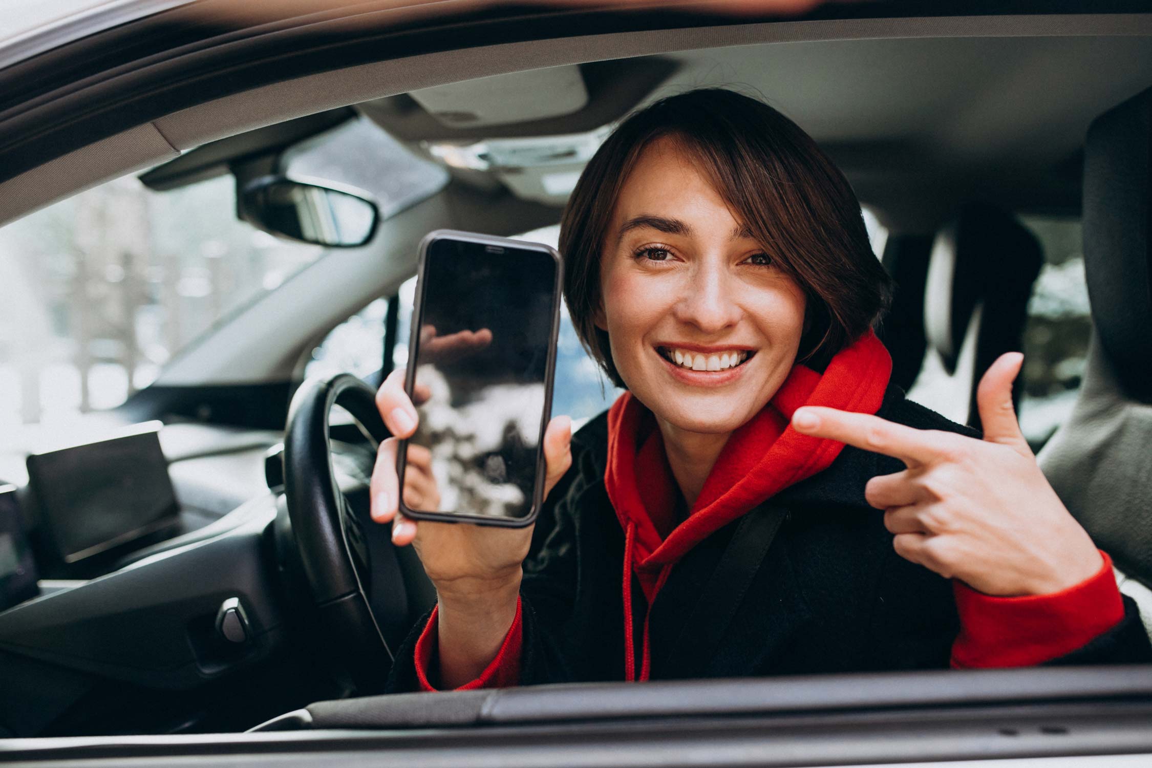 Girl in a rental car smiles while pointing to a smartphone