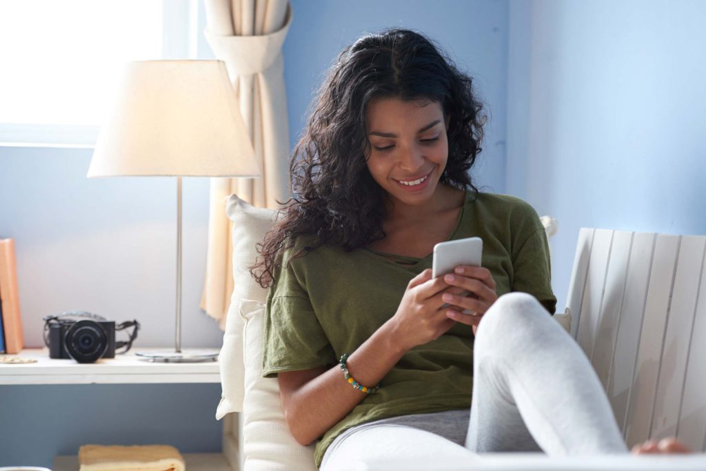 Young woman texting with her smartphone sitting on the sofa of a vacation home